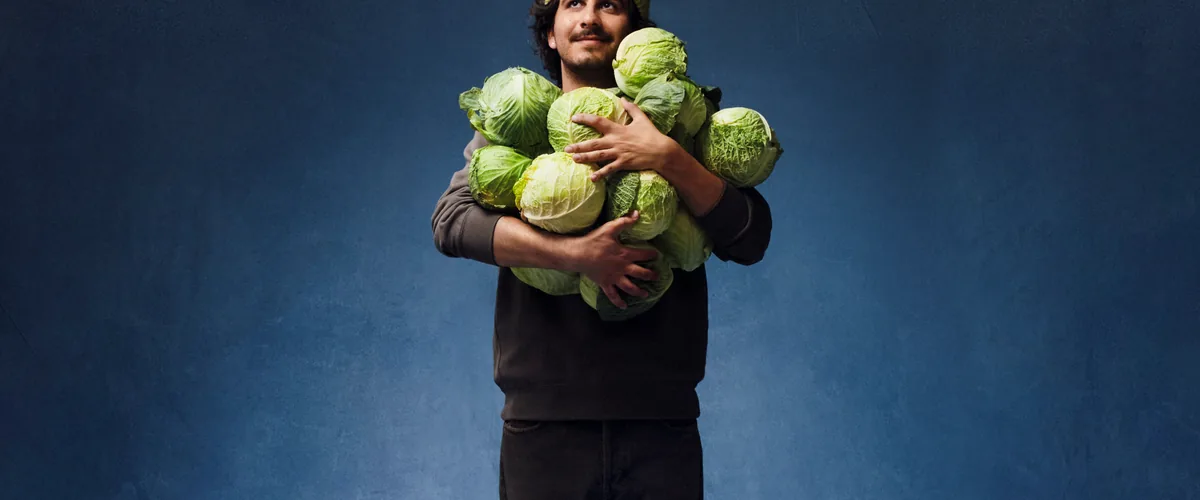 A person in a green knit cap holding an armful of cabbages.